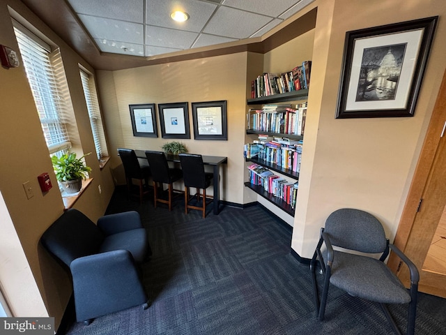 sitting room with a drop ceiling, built in features, and dark carpet