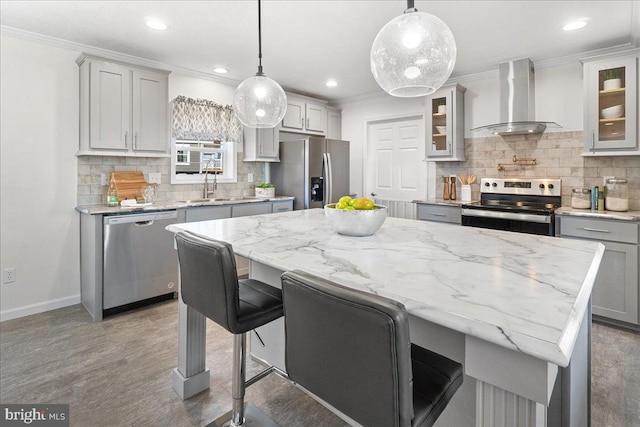 kitchen featuring wall chimney range hood, hanging light fixtures, sink, a center island, and appliances with stainless steel finishes