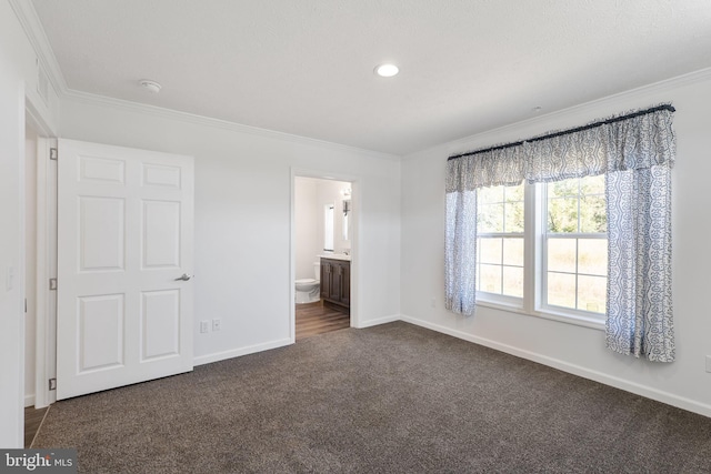 unfurnished bedroom with ensuite bath, ornamental molding, and dark carpet