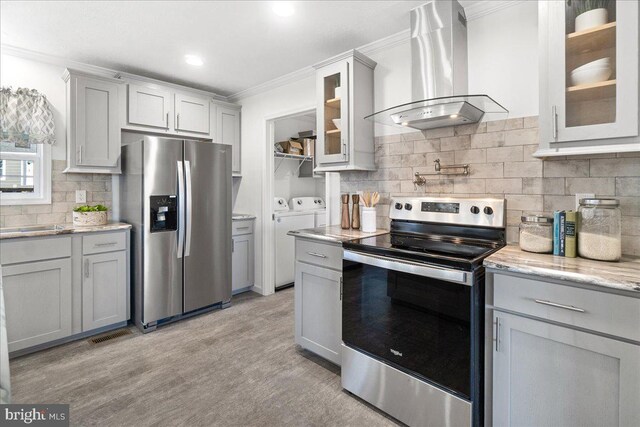 kitchen with wall chimney range hood, gray cabinetry, independent washer and dryer, and stainless steel appliances