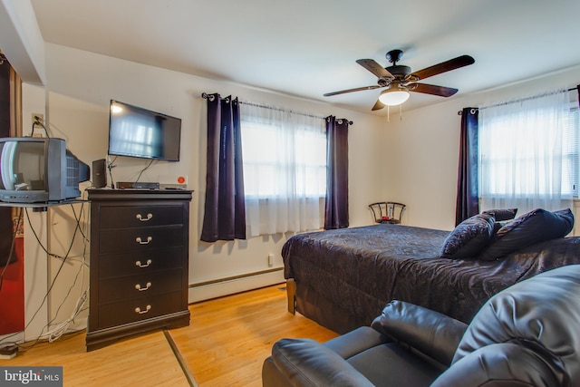 bedroom featuring ceiling fan, a baseboard radiator, light wood-type flooring, and multiple windows