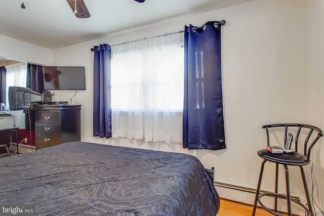 bedroom featuring light hardwood / wood-style floors, multiple windows, baseboard heating, and ceiling fan