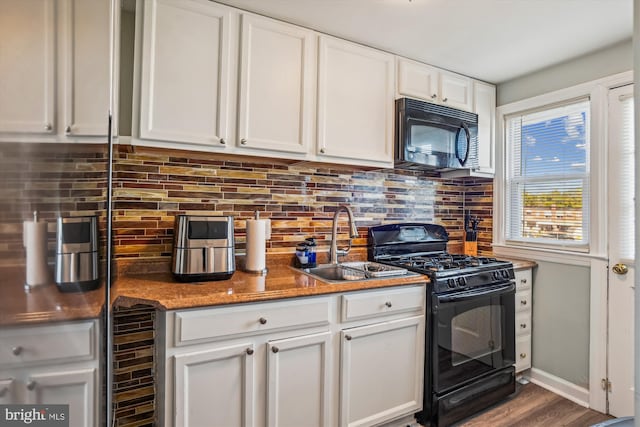 kitchen featuring dark stone counters, hardwood / wood-style floors, sink, black appliances, and white cabinetry