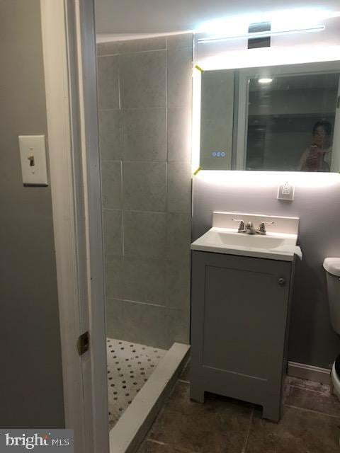 bathroom with tiled shower, vanity, toilet, and tile patterned flooring