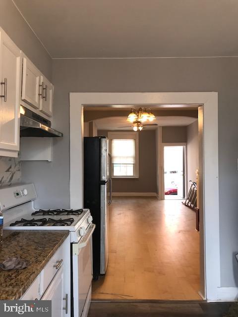 kitchen featuring white cabinets, stainless steel refrigerator, white gas stove, dark stone counters, and hardwood / wood-style floors