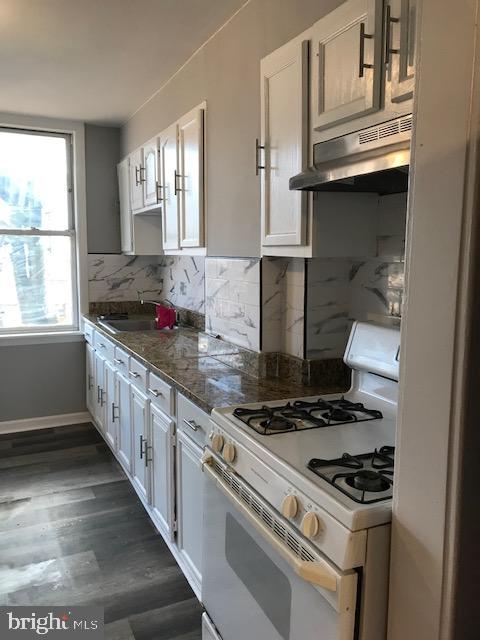 kitchen with backsplash, white cabinets, range hood, and gas range gas stove