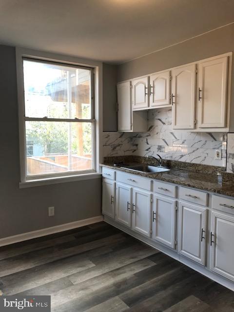 kitchen with dark stone countertops, white cabinetry, tasteful backsplash, dark hardwood / wood-style flooring, and sink