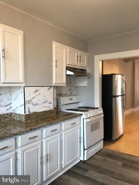 kitchen featuring stainless steel refrigerator, dark wood-type flooring, white gas range oven, and white cabinets