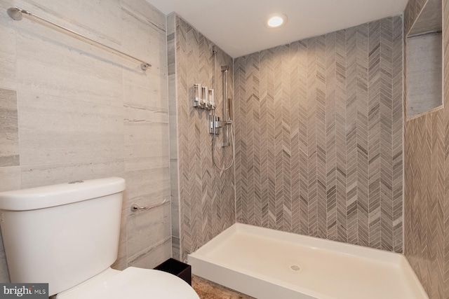 bathroom with tile walls, tiled shower, and toilet