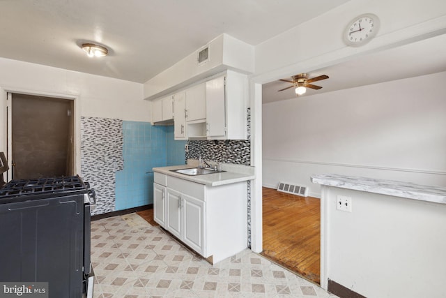 kitchen featuring ceiling fan, white cabinets, black gas range, sink, and light hardwood / wood-style flooring