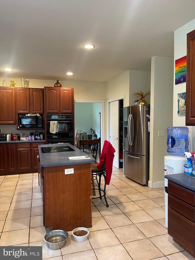 kitchen featuring light tile patterned flooring, a center island, black appliances, and a kitchen bar