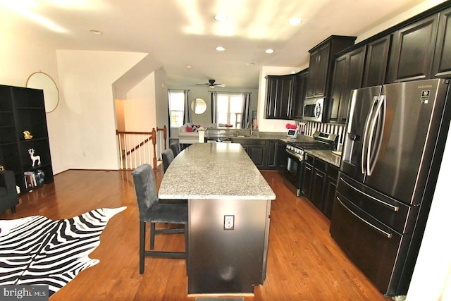 kitchen featuring a breakfast bar area, stainless steel appliances, wood-type flooring, light stone countertops, and a center island