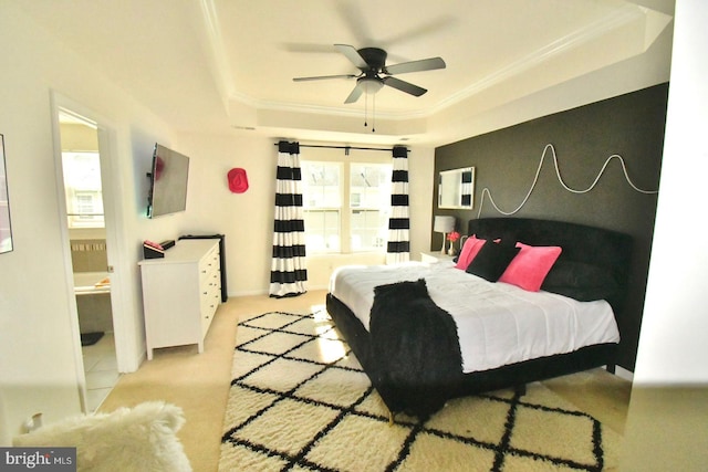 bedroom with a tray ceiling, ensuite bath, ornamental molding, light colored carpet, and ceiling fan