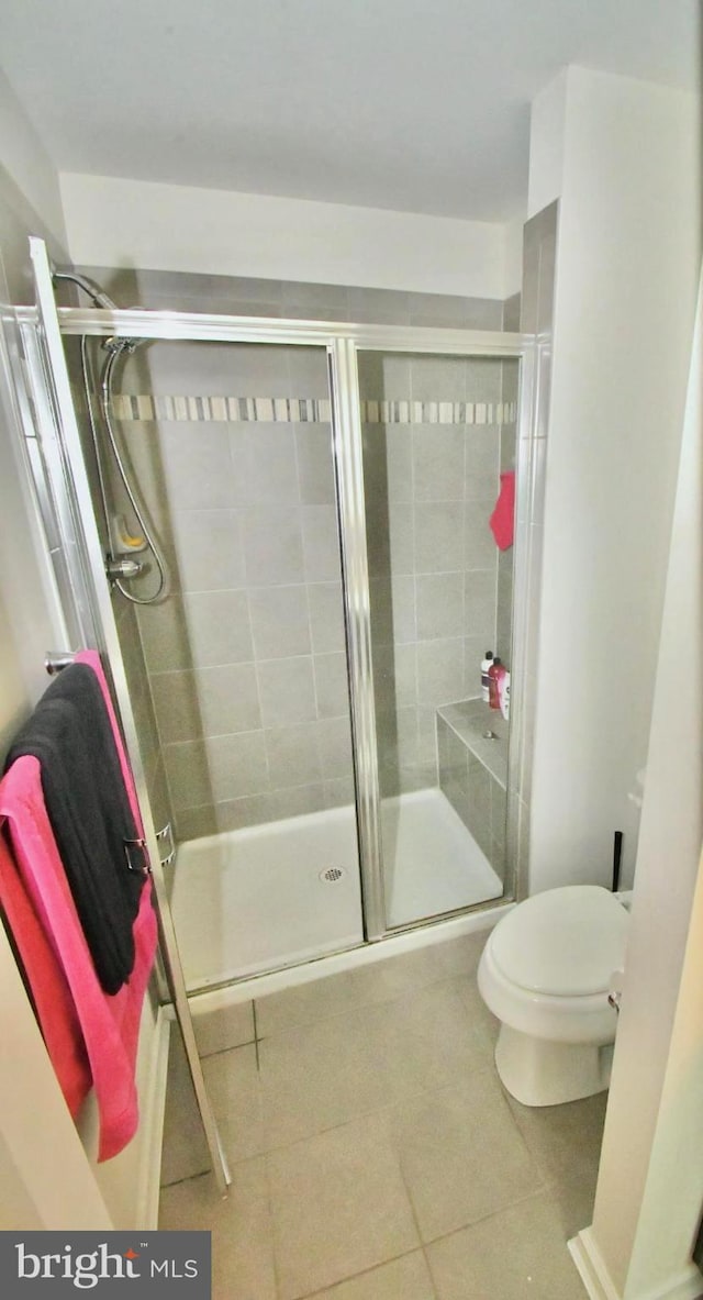 bathroom featuring a shower with door, toilet, and tile patterned floors