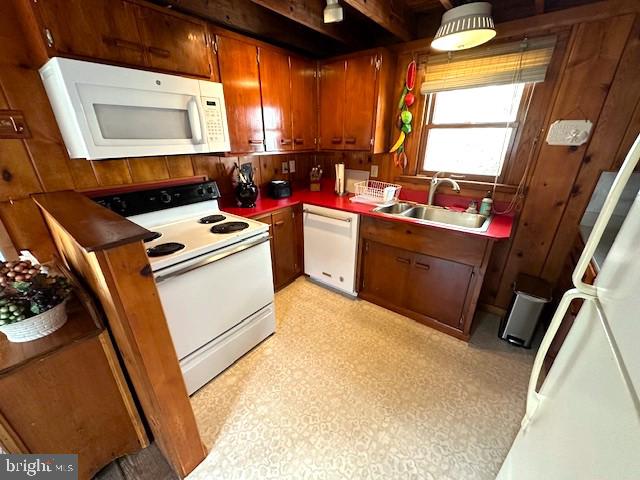 kitchen with beam ceiling, wood walls, white appliances, and sink