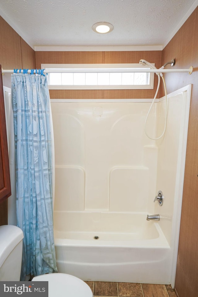 bathroom featuring a textured ceiling, wood walls, toilet, and a wealth of natural light