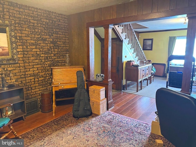 interior space featuring hardwood / wood-style floors, wood walls, a textured ceiling, brick wall, and decorative columns