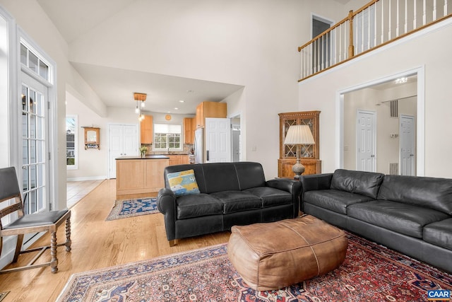 living area with high vaulted ceiling, baseboards, and light wood-style flooring