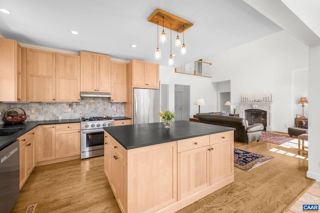 kitchen featuring light brown cabinets, dark countertops, appliances with stainless steel finishes, backsplash, and under cabinet range hood