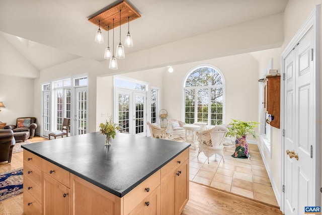 kitchen featuring dark countertops, vaulted ceiling, light brown cabinets, and open floor plan