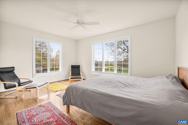 bedroom featuring wood finished floors, a ceiling fan, baseboards, and multiple windows