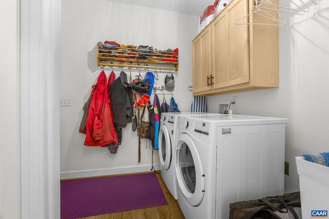 washroom featuring washing machine and dryer, baseboards, wood finished floors, and cabinet space