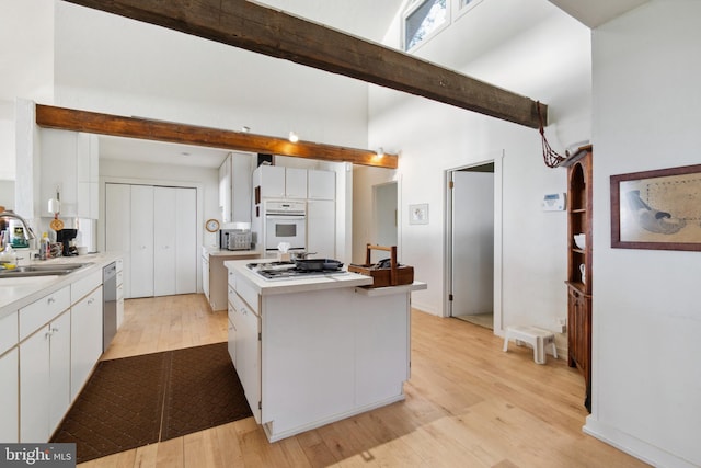 kitchen with appliances with stainless steel finishes, beamed ceiling, light hardwood / wood-style flooring, and white cabinets