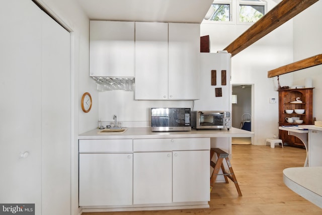 kitchen with light wood-type flooring, white cabinetry, sink, and a breakfast bar