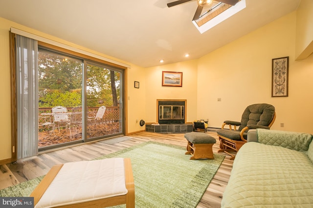 living room with wood-type flooring, a tiled fireplace, lofted ceiling with skylight, and ceiling fan