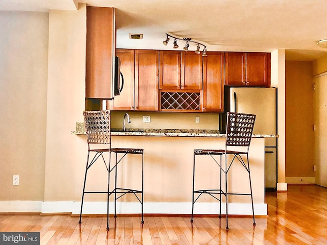 kitchen with kitchen peninsula, sink, a breakfast bar, light wood-type flooring, and stainless steel refrigerator