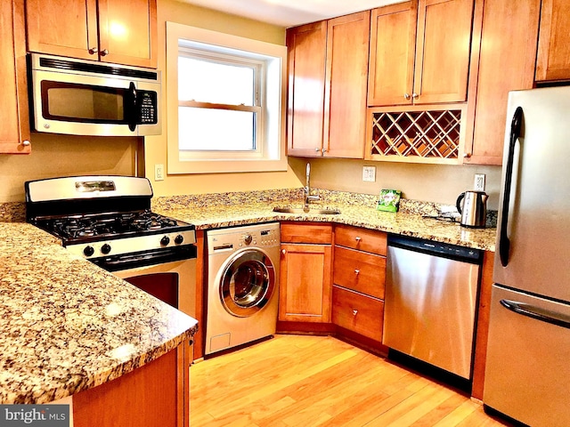 kitchen with washer / dryer, light stone countertops, appliances with stainless steel finishes, sink, and light wood-type flooring