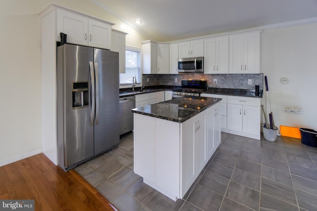 kitchen with stainless steel appliances, dark stone countertops, sink, a center island, and white cabinets