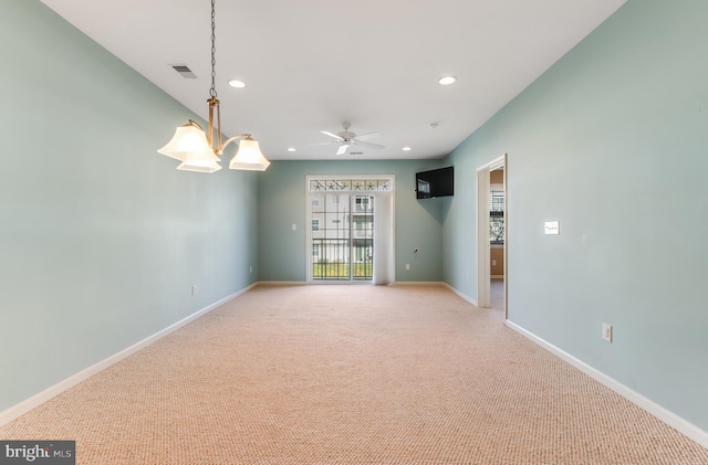 carpeted spare room featuring ceiling fan with notable chandelier