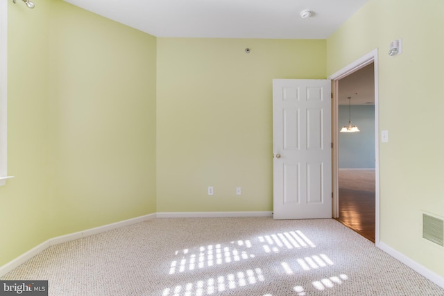 carpeted empty room featuring an inviting chandelier