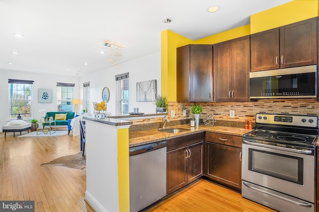 kitchen with kitchen peninsula, appliances with stainless steel finishes, light wood-type flooring, dark stone counters, and sink