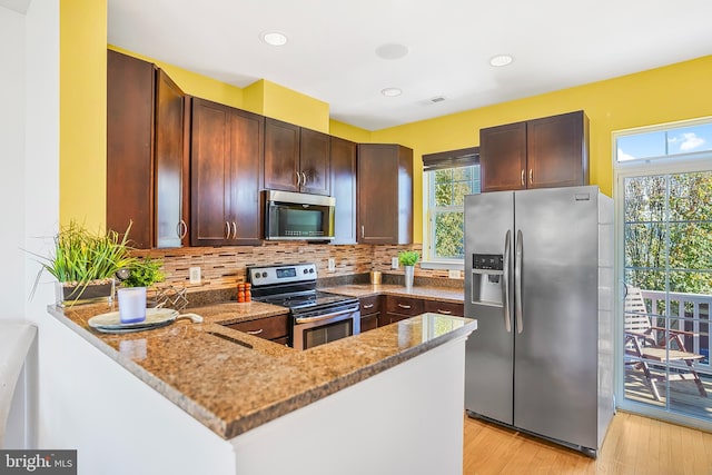 kitchen with light stone countertops, appliances with stainless steel finishes, tasteful backsplash, light hardwood / wood-style floors, and kitchen peninsula