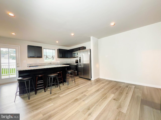 kitchen with appliances with stainless steel finishes, a kitchen bar, light stone counters, and light hardwood / wood-style floors