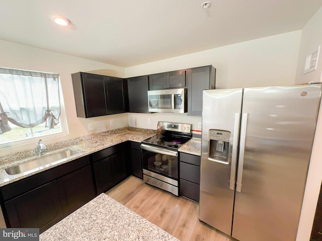 kitchen with stainless steel appliances, sink, light wood-type flooring, and light stone counters