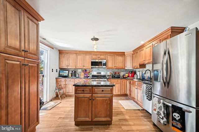 kitchen with a kitchen island, dark stone countertops, sink, light wood-type flooring, and appliances with stainless steel finishes