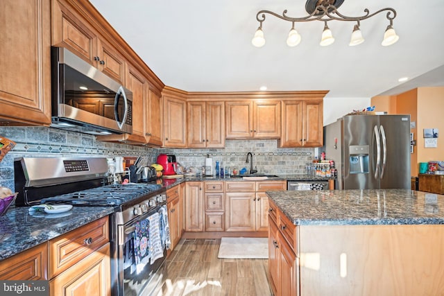 kitchen with tasteful backsplash, dark stone countertops, sink, light hardwood / wood-style floors, and stainless steel appliances