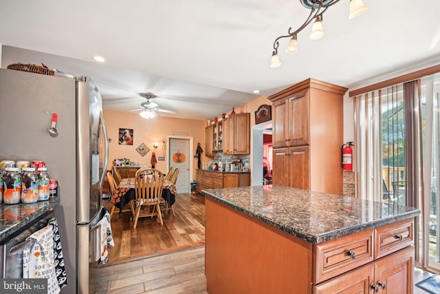 kitchen featuring a center island, stainless steel fridge, ceiling fan, dark stone counters, and light hardwood / wood-style flooring