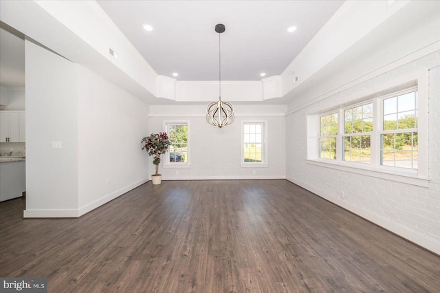 empty room featuring an inviting chandelier, brick wall, and dark hardwood / wood-style flooring