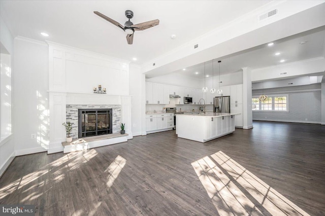 unfurnished living room featuring a stone fireplace, dark hardwood / wood-style floors, sink, and crown molding