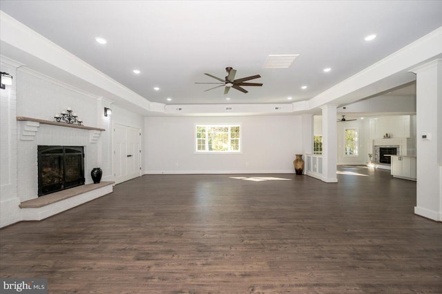 unfurnished living room with ceiling fan, a tray ceiling, dark wood-type flooring, a fireplace, and ornamental molding