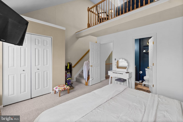 carpeted bedroom featuring a towering ceiling, ensuite bathroom, and a closet