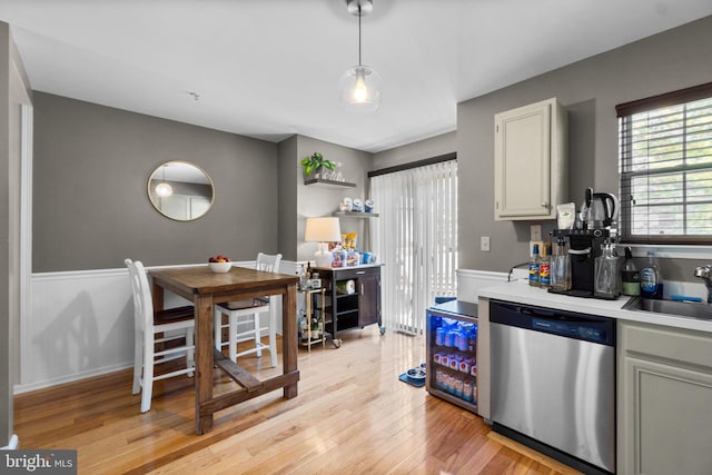 kitchen featuring hanging light fixtures, sink, stainless steel dishwasher, white cabinetry, and light hardwood / wood-style floors