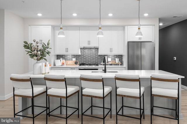 kitchen featuring stainless steel fridge, backsplash, an island with sink, light hardwood / wood-style flooring, and sink