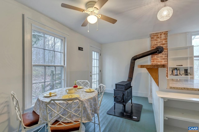 dining room with wood-type flooring, a wood stove, and ceiling fan