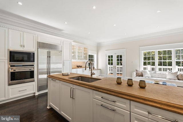 kitchen with built in appliances, white cabinetry, and sink