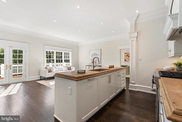 kitchen with wood counters, french doors, stainless steel gas stove, white cabinetry, and an island with sink